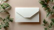 © RizalAziz - Elegant White Envelope Surrounded by Greenery on a Beige Background Flat Lay
