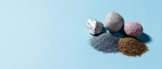 Leinwandbilder - Artistic arrangement of metallic mineral elements, including silver, gray, pink, and gold stones with matching powder, on light blue background, evoking calm mood