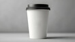 © Anuson - A clean white disposable coffee cup with a black lid stands on a gray background perfect for ing mockups.