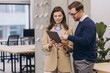 © anatoliycherkas - Two professionals man and woman discussing work on a tablet in a contemporary office setting, surrounded by sticky notes and modern furniture