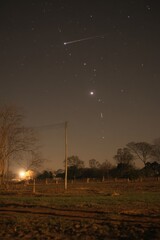 Wall Mural - night sky view of shooting star over rural landscape with power pole and trees in foreground