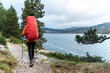 © Rendara Studio - Rear view of solo hiker with red backpack cover walking by mountain lake