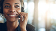 © Frenza - young Black woman customer support agent smiling while taking a call with a headset, clean office background