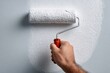 © whitestorm - Painting a wall with a roller covered in white paint to improve the appearance and value, showing the technique of applying a fresh coat of color in a renovation project.