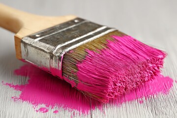 Poster - Bright pink paintbrush resting on a wooden surface with paint splatters in a creative workspace setting