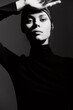 © SHOTPRIME STUDIO - Stylish woman in a black turtleneck posing with one hand raised, showcasing confidence and elegance against a minimalistic dark background.