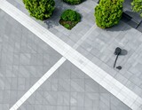 Aerial view of a modern plaza with gray and white stone paving, featuring geometric patterns and lush green shrubs.