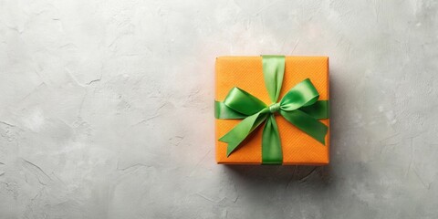 Poster - A vibrant orange gift box adorned with a bright green ribbon bow sits elegantly on a textured gray surface, ideal for celebratory announcements or festive greetings.