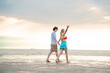 © Wanwajee - Couple laughing together while walking along the coast, sun setting shining above, creating a warm and inviting scene. Ideal for happiness and outdoor lifestyle themes.