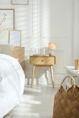 Poster - Bedside table with lamp, jug of water and glass near bed in room. Interior design