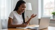 © alleb - Woman smiles writing notes during a video call on a laptop computer.