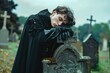 © ECLIVN - A young male, with wavy dark hair, dressed in a long black cloak, mourns beside an old grave, evoking a somber and reflective mood in a misty graveyard.