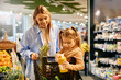 © Valerii Apetroaiei - Little girl holding juice bottle in shopping cart with mother in supermarket aisle