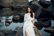 © SHOTPRIME STUDIO - Serene woman in white dress sitting on oceanfront rock gazing at the sea with rocky background
