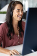 © fizkes - Hybrid communication. Happy laughing young woman teacher in wireless headset with microphone having fun on virtual lesson talking via videocall with student search information with ai using desktop pc