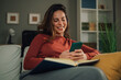 © Zamrznuti tonovi - Woman relaxing on sofa using smartphone and reading book