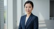 © João Salgado - An asian businesswoman in a dark suit poses gracefully in a bright, modern office.