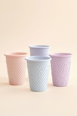 Poster - Pastel Colored Cups Arranged on Beige Background Studio Shot of Four Modern Textured Tumblers in Pink Purple and Blue Colors for Drinkware Mockup