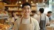© Surachetsh - Smart male baker wearing an apron greets warmly inside a boutique bakery, where fresh pastries and a bright atmosphere highlight the lively small business feel.