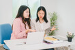 © R Photography - Two Asian businesswoman are engaged in a productive discussion at a modern office table, using a laptop and documents, exchanging ideas, and working together in a bright, professional environment
