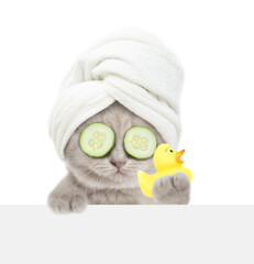Fototapete - Cute kitten with towel on it head and with slices of cucumber on it eyes looks above blank white banner and shows rubber duck. Empty space for text. isolated on white background