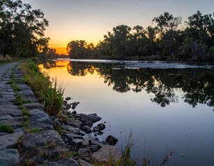 Wall Mural - serene river at sunset, reflecting vibrant colors on water surface, surrounded by lush trees and roc
