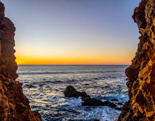 Wall Mural - stunning view of ocean framed by rocky cliffs at sunset, showcasing vibrant colors in sky and gentle waves lapping against shore. scene evokes sense of tranquility and natural beauty