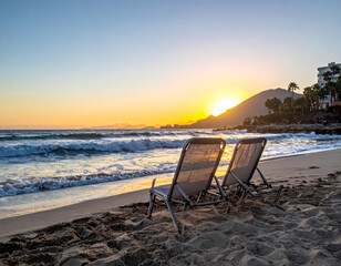 Wall Mural - Relaxing beach scene with two chairs facing ocean at sunset, capturing serene beauty of nature and calming waves. perfect spot for unwinding and enjoying view