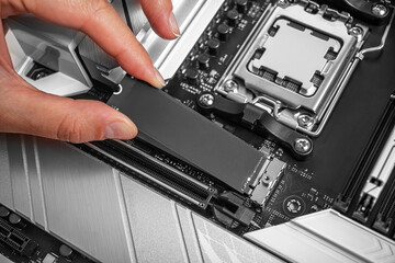 Poster - A person is installing an M.2 NVMe SSD into a modern motherboard socket, showcasing computer hardware assembly in progress.