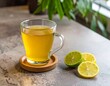 © feridaydin - Glass mug with yellow drink, lime and lemon slices beside it, green plant in relaxed background.