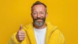 © Blackmint Studio - Happy older man wearing a casual yellow sweater enjoys the moment, proudly giving a thumbs up. His cheerful expression radiates positivity and delight