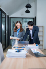 Poster - Two Asian businesspeople collaborating in an office, analyzing financial data while working on a laptop and reviewing important documents for effective decision-making