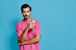© SHOTPRIME STUDIO - Confident smiling man in pink t-shirt holds smartphone while posing against vibrant turquoise background, exuding modern lifestyle and tech-savvy vibe.