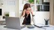 © wattana - Stressed businesswoman holding her head in pain at office desk, struggling with workload and deadlines.