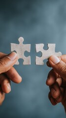 Poster - Close up of hands holding two puzzle pieces about to connect on a blue background conceptual of teamwork solution and strategy