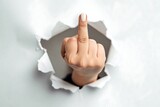 Female hand making rude gesture through torn paper – provocative concept