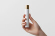 © Wizard - Hand holding white bottle gold cap beauty product minimalist design