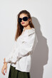 © SHOTPRIME STUDIO - Fashion model wearing a stylish white shirt and sunglasses, posing against a plain light background to highlight her outfit and confident posture