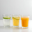 © Hamza - Three glasses filled with different drinks, one with lime, on a white surface, studio shot