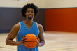 © WavebreakMediaMicro - African American man standing on gym basketball court, holding basketball and smiling at camera