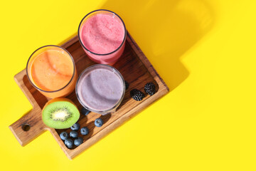 Wall Mural - Glasses of fresh smoothie with different berries on yellow background