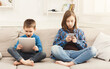 © Prostock-studio - Two kids with gadgets. Sister and brother surfing the net or playing online games on smartphone and digital tablet at home. Modern communication and gadget addiction concept