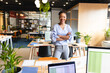© Wavebreak Media - African American woman standing confidently in modern office with crossed arms and laptops visible
