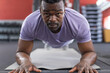 © Wavebreak Media - African American man holding forearm plank on gray mat in gym, with dumbbell rack, step platforms