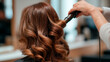 © Simone Matos - Stylist curls shiny brunette hair with a curling iron for a glamorous wavy look.