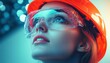 © Donna - confident woman wearing orange safety helmet and transparent protective goggles looking upward with determination
