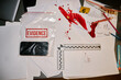© Seventyfour - Evidence bag containing phone with spilled blood on papers and crime scene marker nearby, along with ruler and pens. Scene arranged on dark reflective table