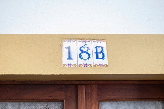Decorative Tile House Number 18B. Close-up of ornate ceramic tiles displaying the blue house number '18B' with floral designs, mounted on a light brown wall above a dark wooden door