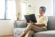 © khwanchai - An elderly Thai woman has eye pain, farsightedness while reading a book, and is sitting on a sofa at home