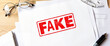 © Anastasiya - Red FAKE stamp on documents in simple workspace, document authenticity